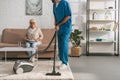 cropped shot of social worker cleaning carpet with vacuum cleaner while senior woman