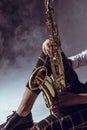 cropped shot of stylish musician holding saxophone in smoke