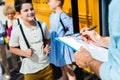 cropped shot of teacher writing in list on clipboard while pupils entering at school bus blurred