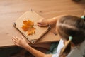 Cropped shot of thoughtful little child girl holding beautiful dry maple leaf to create herbarium diy at home. Royalty Free Stock Photo