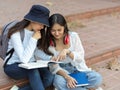 Two young female university students reading together and  sharing an idea while outdoor studying at staircase Royalty Free Stock Photo