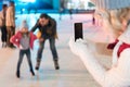 cropped shot of woman holding smartphone with blank screen and photographing family skating