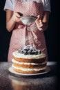 cropped shot of woman spilling sugar powder onto tasty blackberry