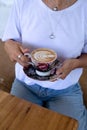 cropped shot of Woman in white shirt holding cup of hot cappuccino on wooden table, top view. Royalty Free Stock Photo