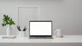 Cropped shot of workspace with blank screen laptop, frame, pencils, coffee cup and vase on white table with white wall Royalty Free Stock Photo