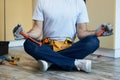 Cropped shot of young handyman holding a hammer and an adjustable wrench in his hands while meditating, sitting in Lotus Royalty Free Stock Photo