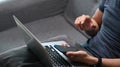 A young man sitting on sofa with laptop computer and using smart phone. Royalty Free Stock Photo