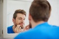 Should I zap this zit or not. Cropped shot of a young man squeezing a pimple in front of a bathroom mirror. Royalty Free Stock Photo