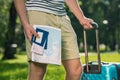 Young tourist with suitcase holding map, passports, tickets and credit card in park