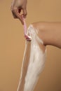 Cropped shot of young woman shaving her leg on beige background Royalty Free Stock Photo