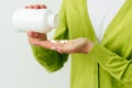 Cropped studio image of woman`s hand pours the pills out of the bottle. Healthy female wearing green cardigan and white t shirt Royalty Free Stock Photo