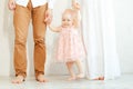 Cropped studio photo of shy, smiling little barefoot baby girl in pink dress stepping and raising leg, hold family arms Royalty Free Stock Photo