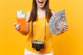 Cropped tourist woman in summer casual clothes holding bundle of dollars money, passport isolated on yellow orange