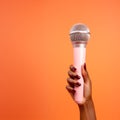 Cropped view of African American woman holding microphone isolated on orange. Royalty Free Stock Photo