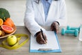 Cropped view of black female dietitian planning meal for client, writing in clipboard, sitting at desk at clinic Royalty Free Stock Photo