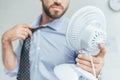 cropped view of businessman cooling himself with electric fan