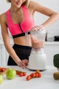 View of cheerful sportswoman preparing smoothie in blender