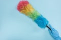 Cropped view of cleaner in rubber glove holding rainbow duster on blue background.