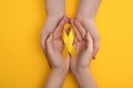 Cropped view of couple holding yellow ribbon on colorful background, international childhood cancer day concept. Royalty Free Stock Photo