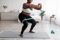 Cropped view of curvy black woman squatting with rubber band on domestic workout