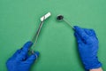 Cropped view of dentist in blue latex gloves holding scissors with cotton pad and medical mirror on green.