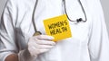 Cropped view of doctor in a white coat and sterile gloves holding a note with text - WOMEN`S HEALTH