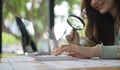 Cropped view of female auditor reading document through magnifying glass and using calculator at her office desk Royalty Free Stock Photo