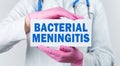 Cropped view of female doctor in a white coat and pink sterile gloves holding a card with words - Bacterial Meningitis