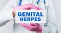 Cropped view of female doctor in a white coat and pink sterile gloves holding a card with words - GENITAL HERPES