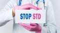 Cropped view of female doctor in a white coat and pink sterile gloves holding a card with words - STOP STD