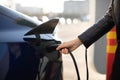 Cropped view of female hand, holding power cable supply plugged in electric car, charging automobile battery from city Royalty Free Stock Photo