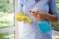Close-up of a housewife spraying detergent on a yellow cloth while washing windows in veranda. Spring cleaning concept