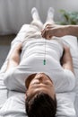 View of hypnotist standing near man on massage table and holding green stone