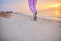 Cropped view of legs in sports shoes of sporty woman running along sea coast against background of beautiful sunrise Royalty Free Stock Photo