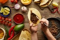 Cropped view of man adding minced meat in taco with raw ingredients on wooden surface Royalty Free Stock Photo