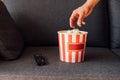 View of man reaching popcorn in bucket near remote controller on sofa