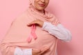 Cropped view. Muslim woman wearing hijab holding pink satin ribbon at chest level to show her support for cancer patients and