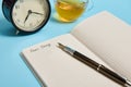 Cropped view of an open notepad with word Dear Diary, alarm clock and an ink pen next to a tea cup on blue background with copy Royalty Free Stock Photo