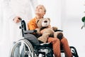 View of pediatrist in white coat and kid with teddy bear on wheelchair