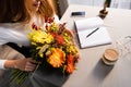 View of redhead woman with bouquet of autumn flowers in cafe with coffee, smartphone and notebook Royalty Free Stock Photo