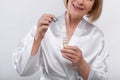 Cropped view of senior woman in dressing gown applying face serum on light studio background, closeup. Skincare concept Royalty Free Stock Photo