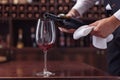 Cropped view sommelier pouring red wine from bottle into glass at table