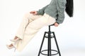 Cropped view of stylish woman in white trousers sits on a wooden black chair on white background Royalty Free Stock Photo