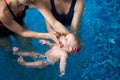 Cropped view of two women trying carefully keeping baby on water. Cute calm little child lying on his back in blue water Royalty Free Stock Photo