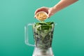 Cropped view of woman adding pine nuts to basil leaves in food processor isolated on green Royalty Free Stock Photo