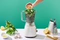 Cropped view of woman adding pine nuts to basil leaves in food processor near pesto sauce raw ingredients on white table isolated Royalty Free Stock Photo