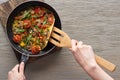Cropped view of woman cooking omelet with mushrooms, tomatoes and greens on frying pan with wooden shovel. Royalty Free Stock Photo