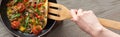 Cropped view of woman cooking tasty omelet with tomatoes and greens on frying pan with wooden shovel. Royalty Free Stock Photo