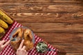 Cropped view of woman cutting roasted turkey on red plaid napkin near grilled corn on wooden table.