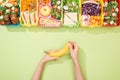 Cropped view of woman holding banana in hands near lunch boxes with food. Royalty Free Stock Photo